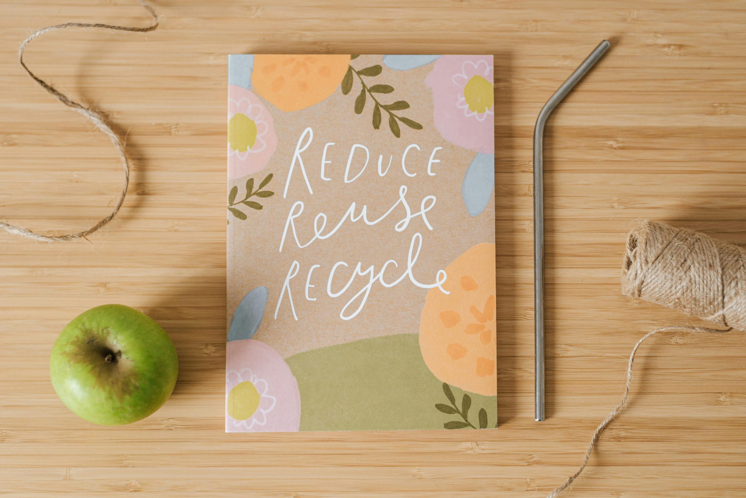 Despre noi Top view of book with Reduce Reuse Recycle inscriptions near green apple and bobbin of thread on table